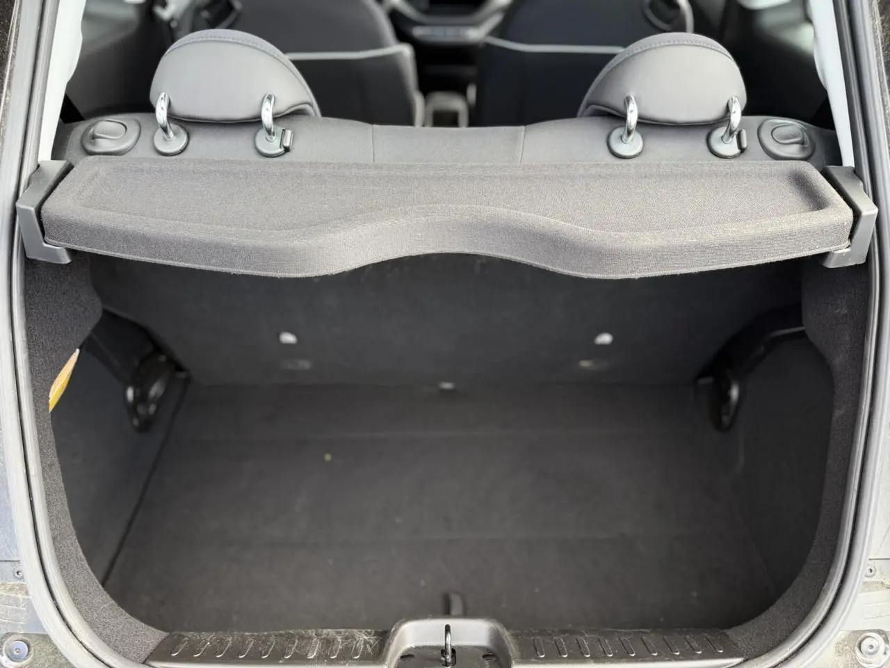 Coffre ouvert vu de l'arrière d'une Fiat 500 électrique blanche, montrant l'espace de chargement et les appuie-têtes arrière.