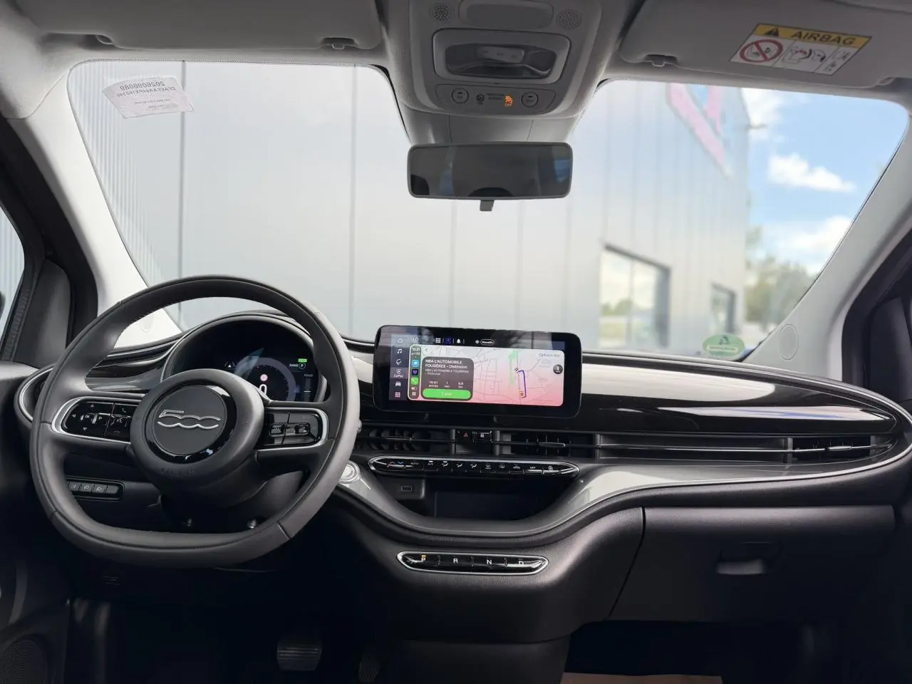 Vue intérieure frontale du tableau de bord noir brillant et volant FIAT 500 électrique avec écran tactile central affichant la navigation.