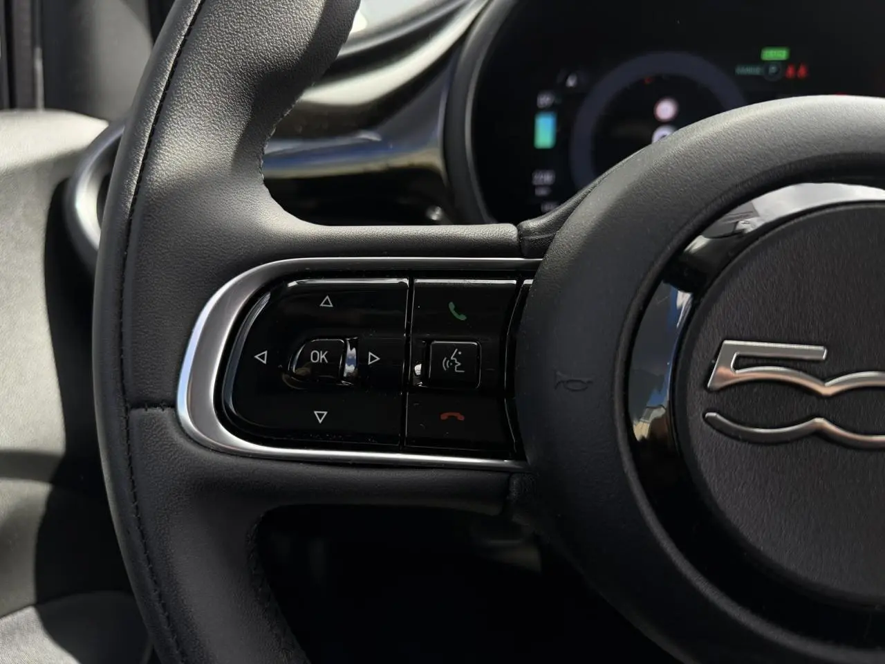 Gros plan sur le volant noir Soft-Touch de la Fiat 500 électrique 2024, avec commandes intégrées et logo 500 au centre.