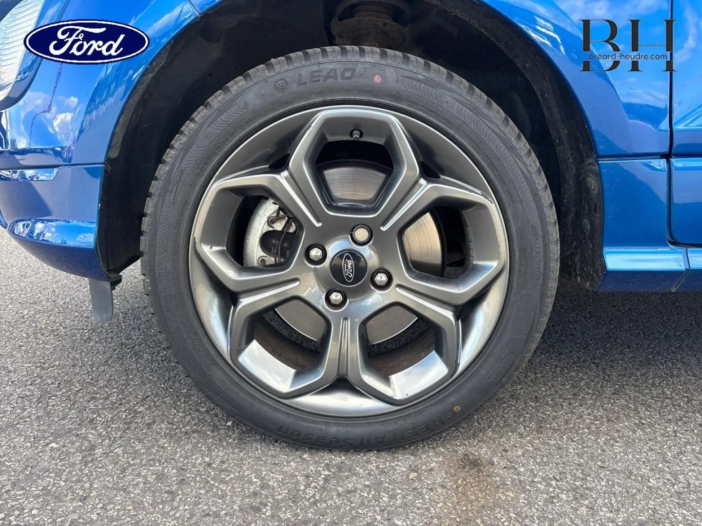 Gros plan sur la roue avant gauche avec jante alu grise du Ford Ecosport bleu Lightning, partie basse de la carrosserie visible.