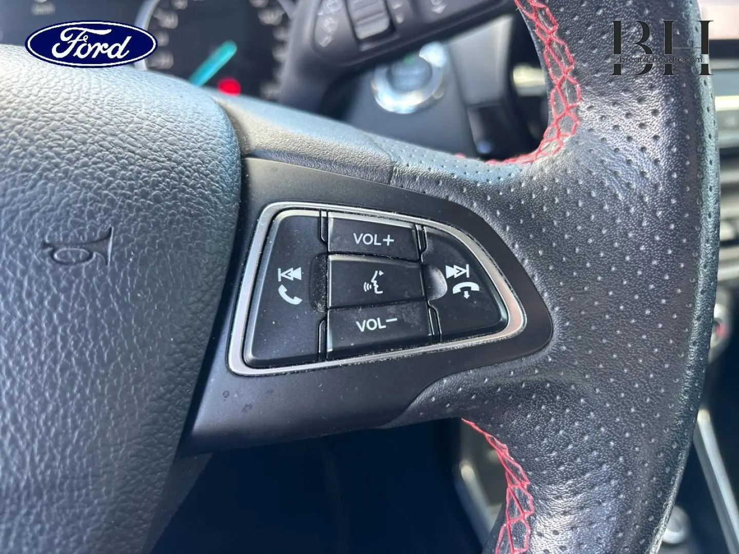 Gros plan sur les commandes de volume et téléphone au volant cuir perforé avec surpiqûres rouges du Ford EcoSport 2018.