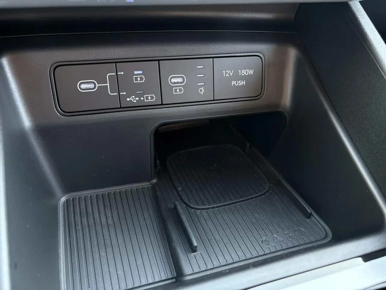 Gros plan sur la console centrale noire du Hyundai Tucson 2025 avec ports USB, prise 12V et chargeur sans fil.