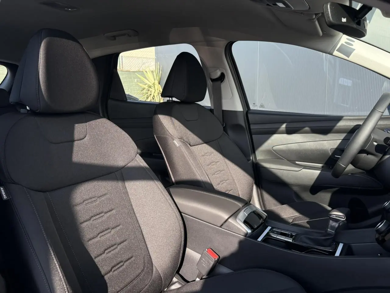Vue intérieure côté droit du Hyundai Tucson 2025, sièges avant en tissu noir avec console centrale et levier de vitesses.