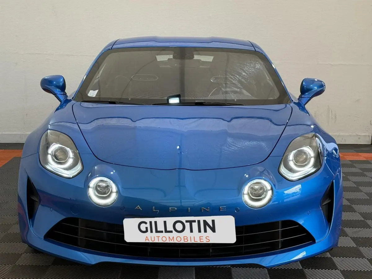Vue frontale de l'Alpine A110 Légende 2019 en bleu, avec ses phares LED ronds caractéristiques allumés.