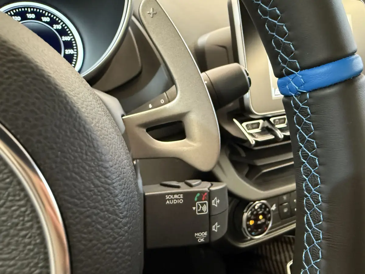 Gros plan sur le volant cuir noir à surpiqûres bleues de l'Alpine A110 Legende 2019 avec tableau de bord et commandes audio.