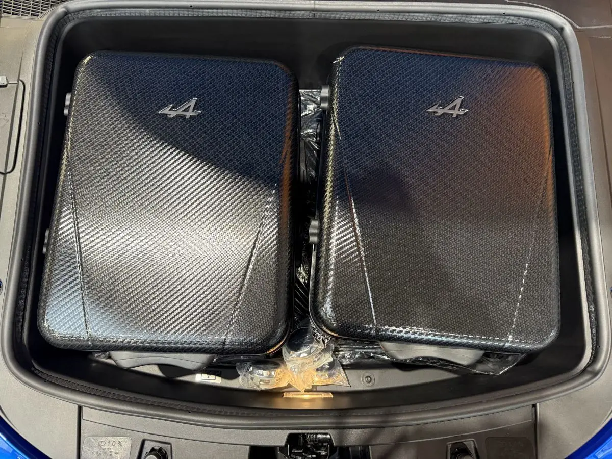 Vue plongeante sur le coffre avant bleu de l'Alpine A110 Legende 2019 avec deux valises noires à motif carbone et logo Alpine.