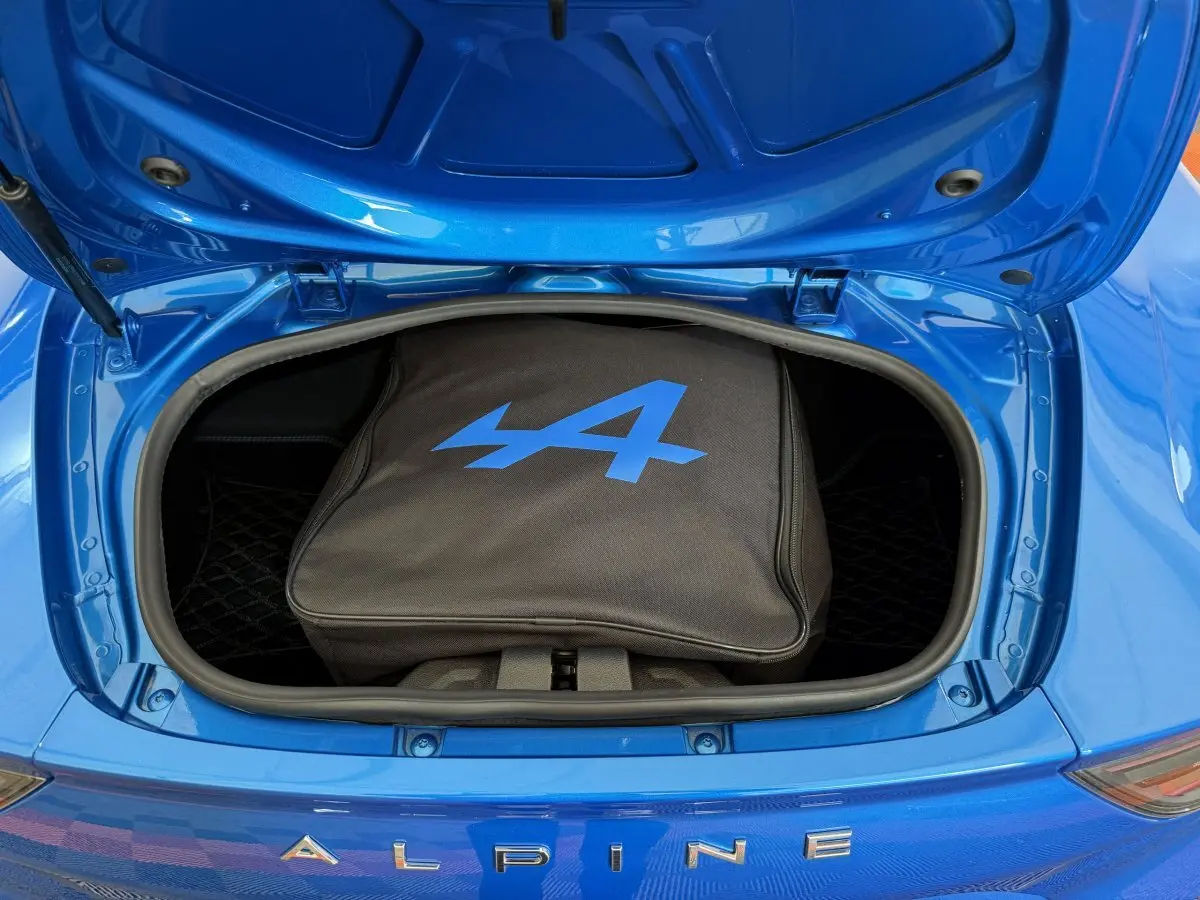 Coffre avant ouvert d'une Alpine A110 Legende bleu 2019, avec sac noir marqué du logo Alpine bleu visible.