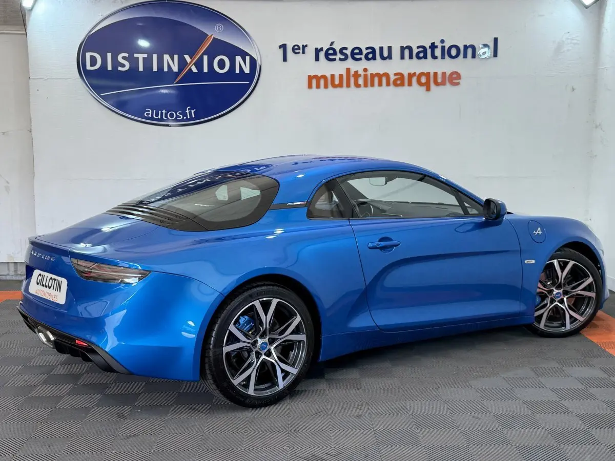 Vue 3/4 arrière droite d'une Alpine A110 Légende bleu brillant avec jantes sport et feux arrière LED dans un showroom.