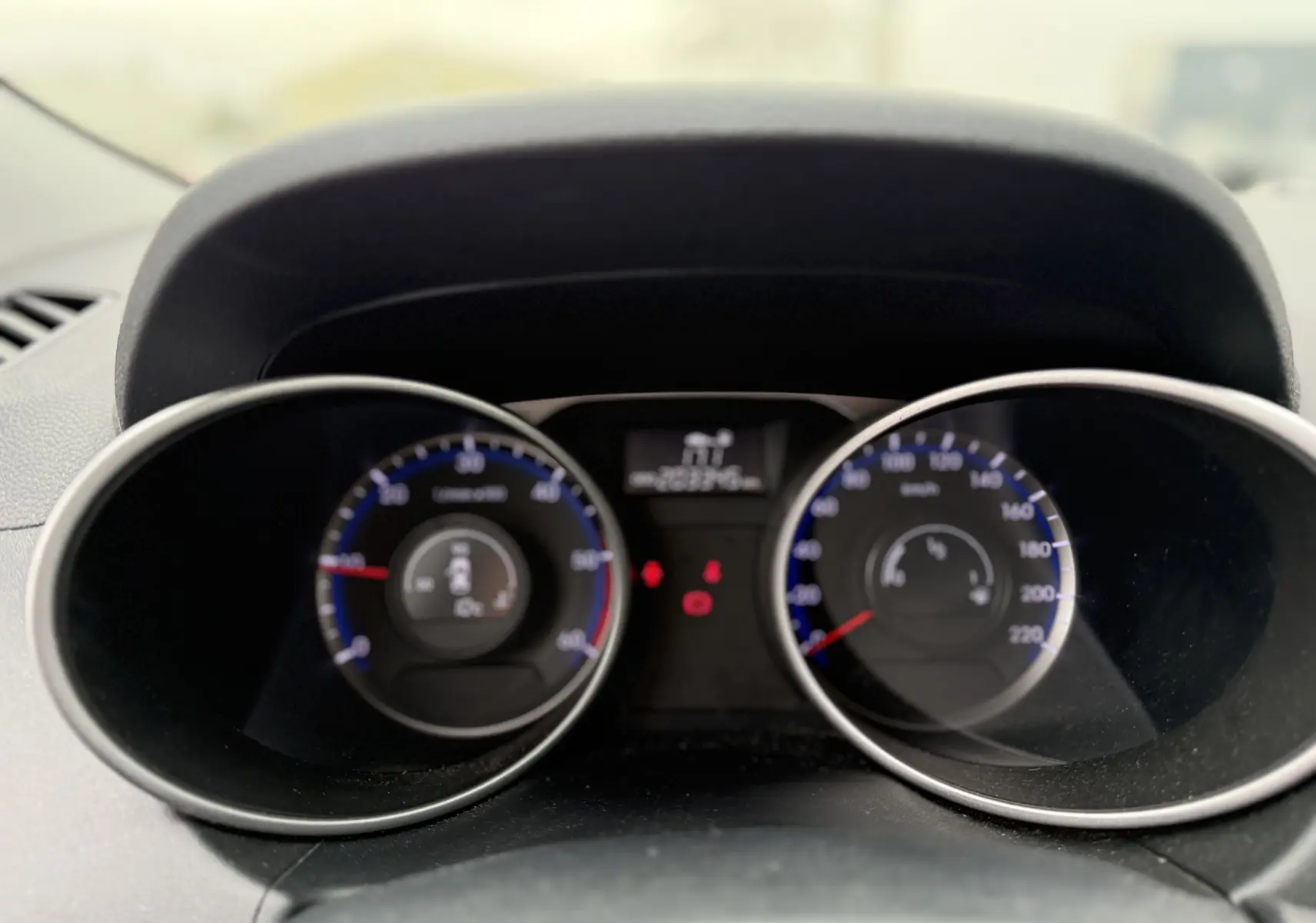 Vue rapprochée du tableau de bord du Hyundai ix35 blanc, avec compte-tours et compteur de vitesse à éclairage bleu.