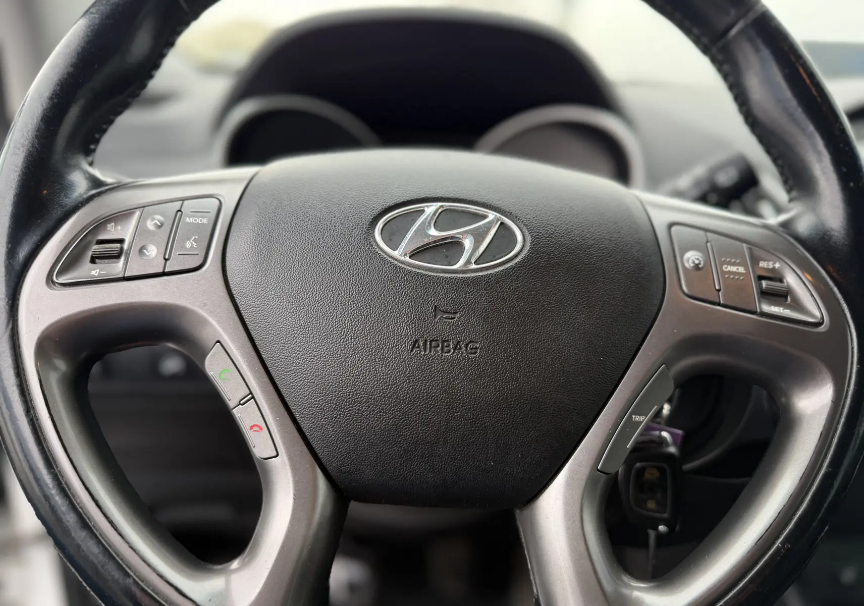 Gros plan sur le volant multifonction noir du Hyundai ix35 2014, avec commandes intégrées et logo central visible.