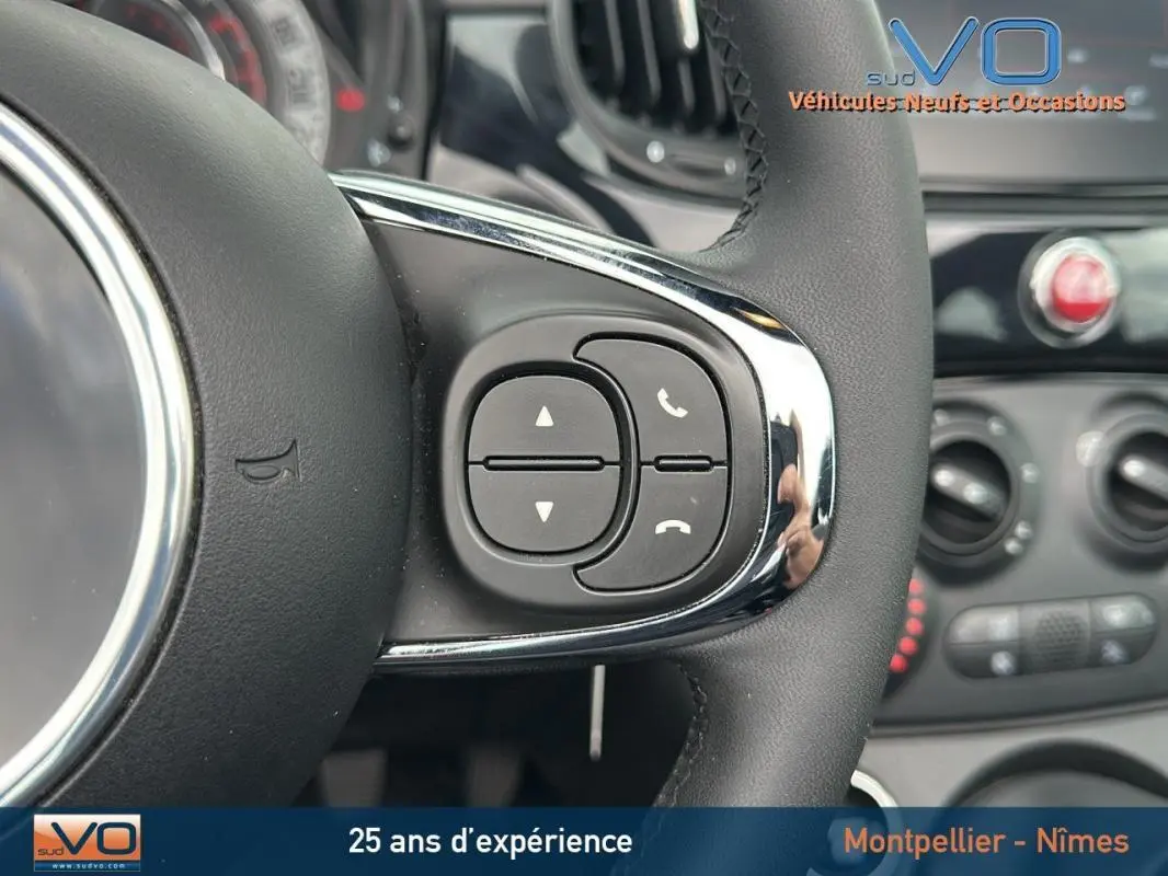 Gros plan sur les commandes au volant côté droit d'une FIAT 500C noire, avec tableau de bord en arrière-plan flou.