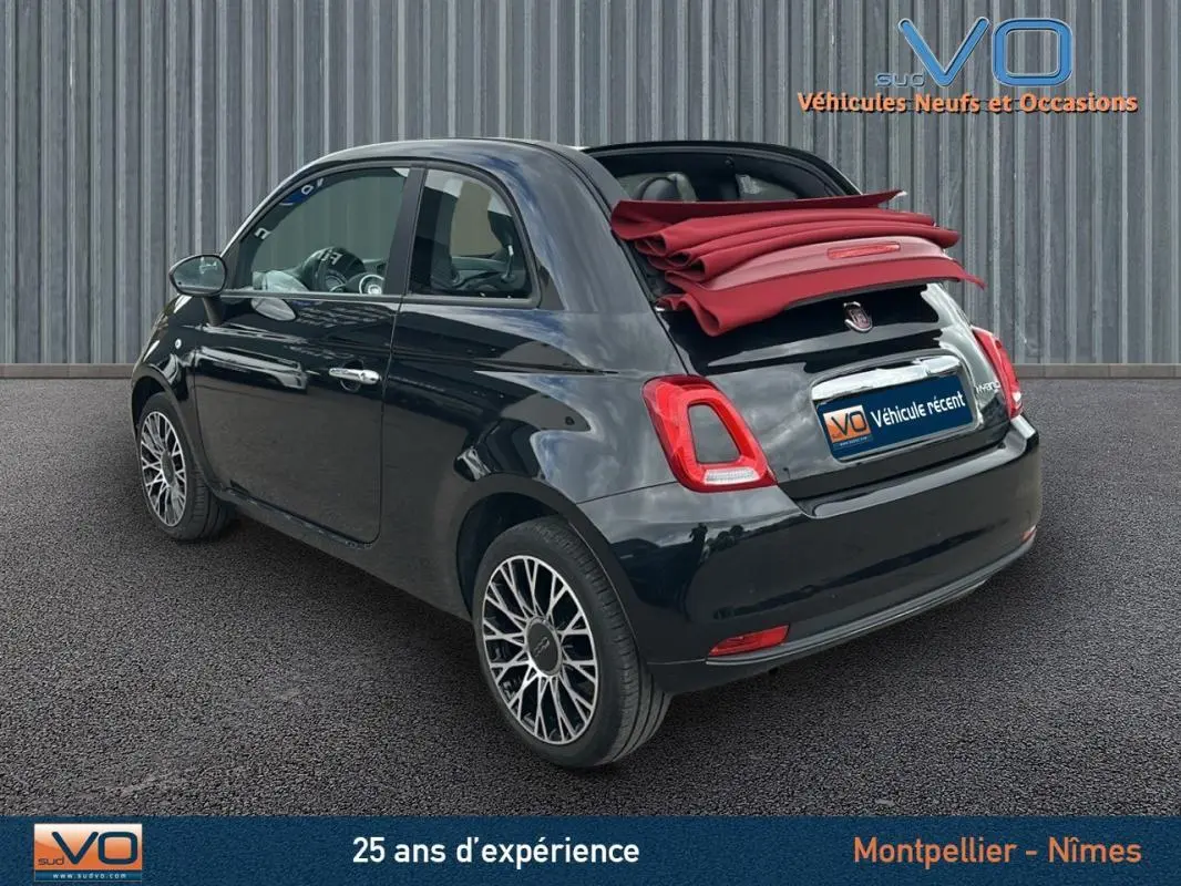 Vue 3/4 arrière droite d'une FIAT 500C noire 2024 avec toit rouge replié et jantes alliage, stationnée sur sol gris.