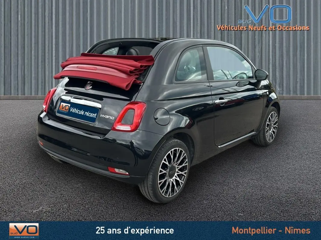Vue 3/4 arrière droite d'une Fiat 500C noire 2024 avec toit rouge décapoté et roue de secours visible.