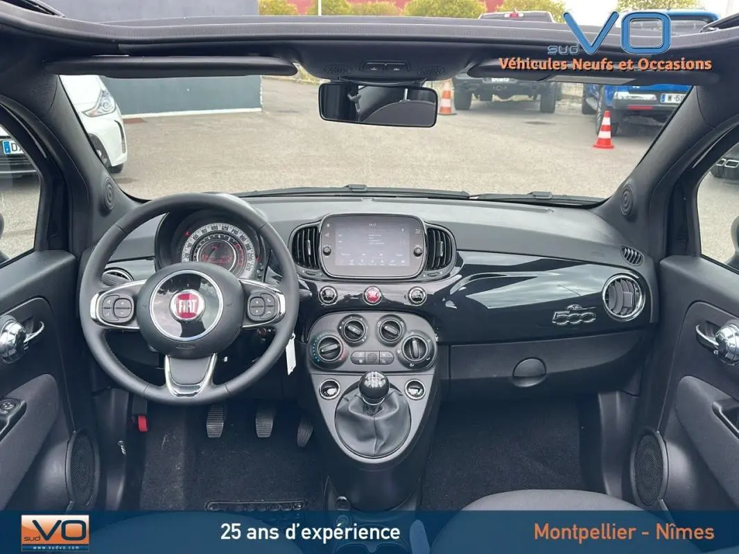 Vue intérieure avant du tableau de bord noir brillant de la FIAT 500C 2024 avec volant multifonction et écran tactile central.