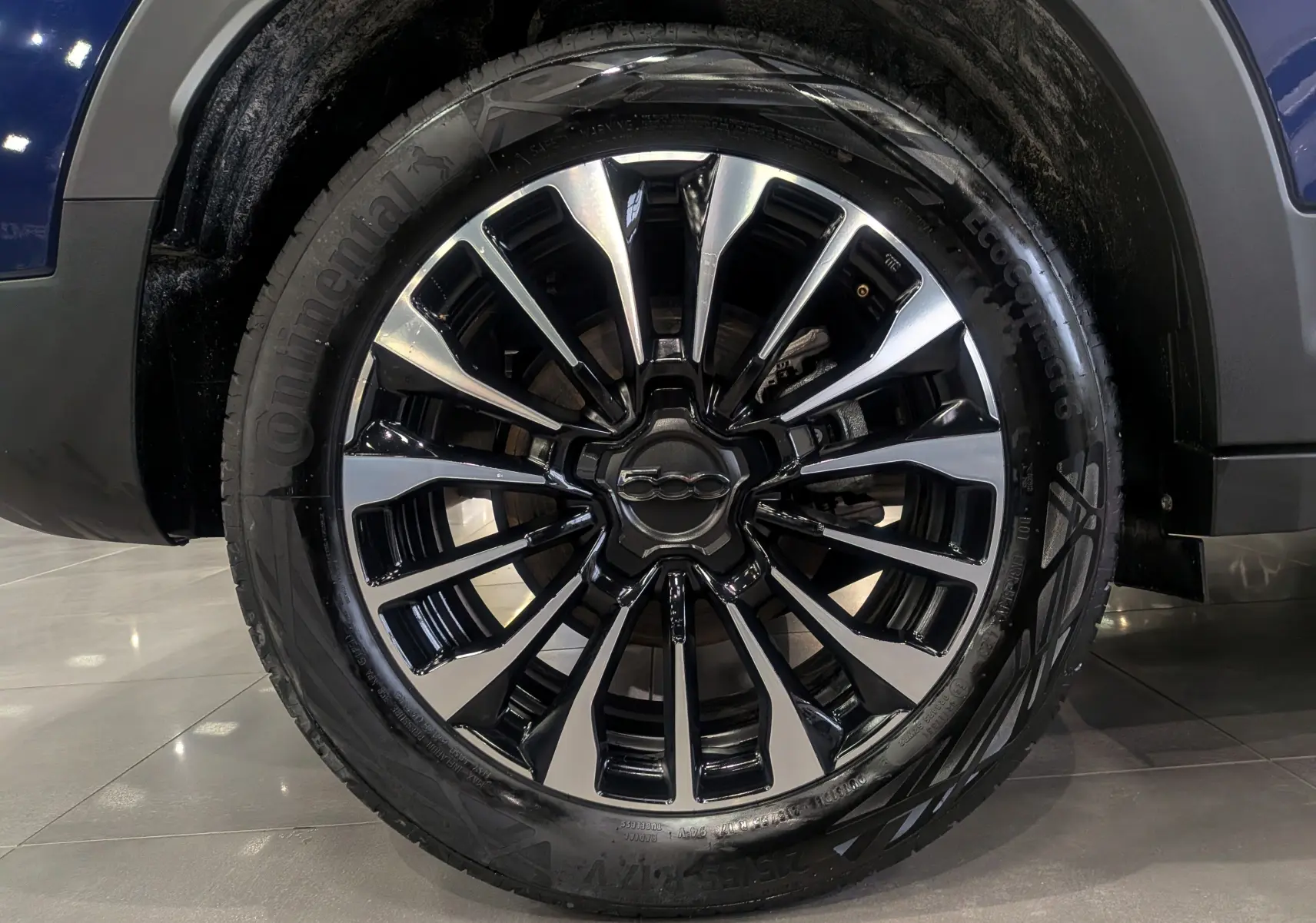 Gros plan sur la roue avant droite d'une FIAT 500X bleu Venezia, mettant en valeur la jante alliage noire et argentée.