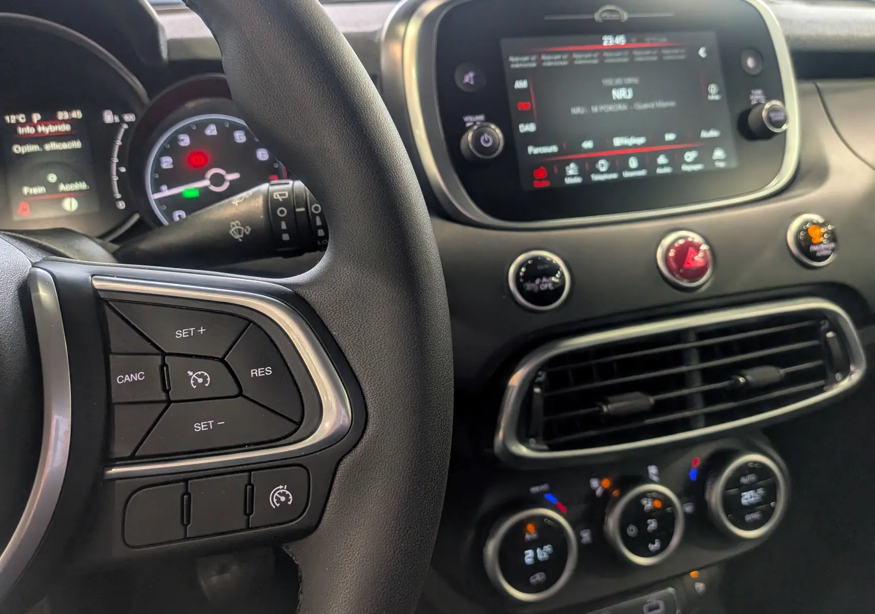 Vue rapprochée de l’intérieur du Fiat 500X bleu Venezia, montrant le volant, l’écran tactile et les commandes de climatisation.