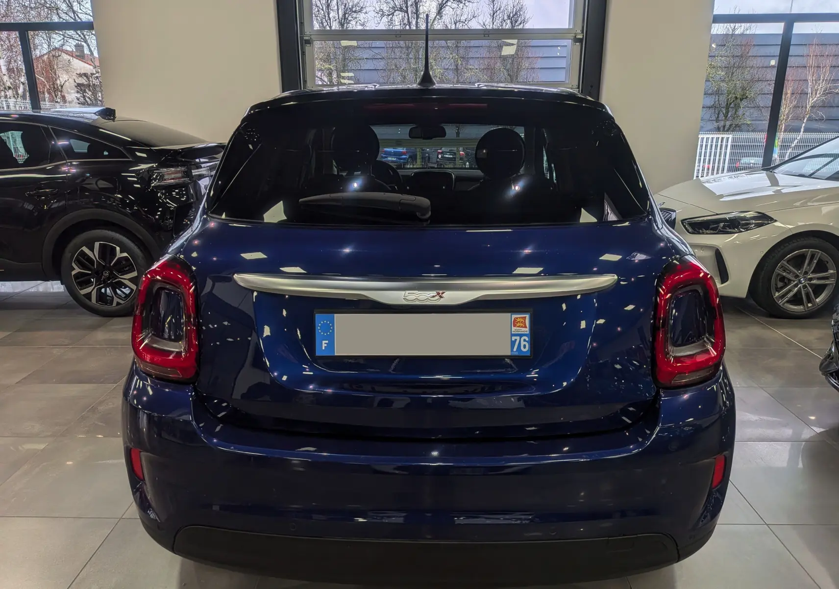 Vue arrière d'une FIAT 500X bleu Venezia 2024 dans un showroom, avec feux arrière rouges et lunette arrière noire.