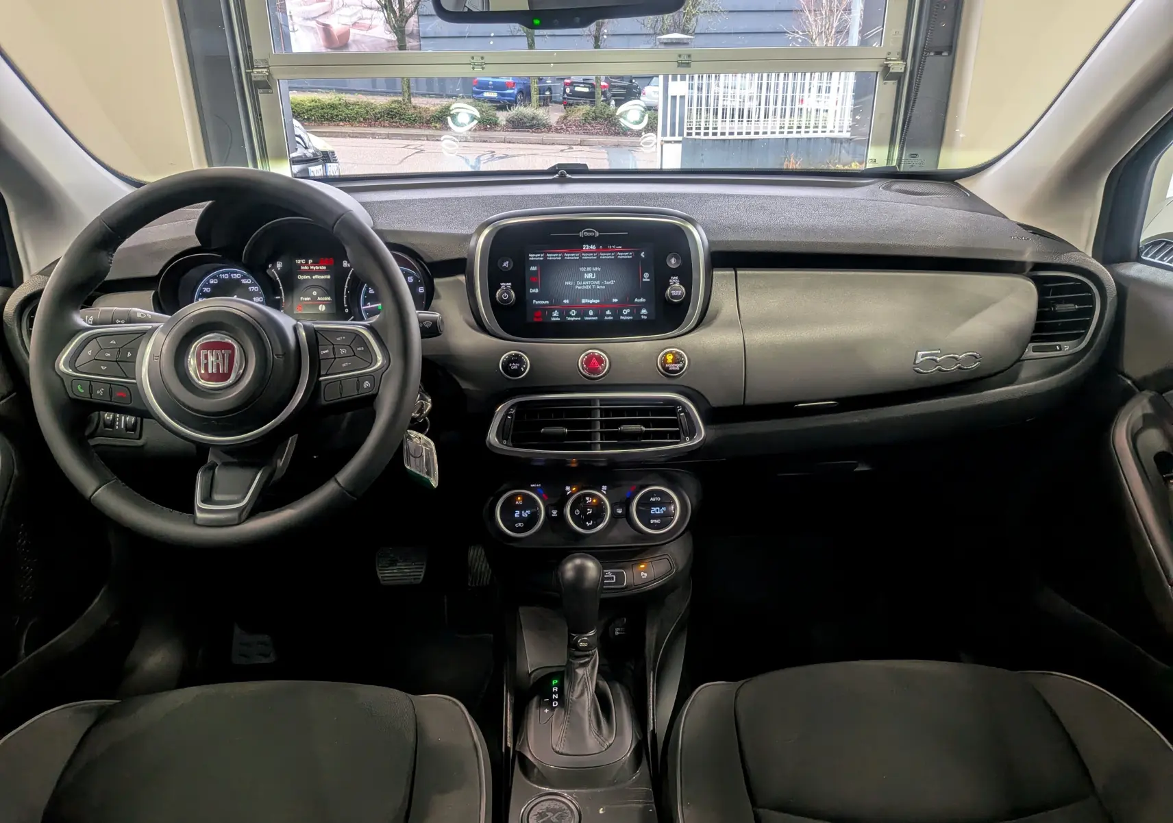 Vue intérieure frontale du tableau de bord noir du Fiat 500X 2024 avec écran tactile central et volant multifonction.