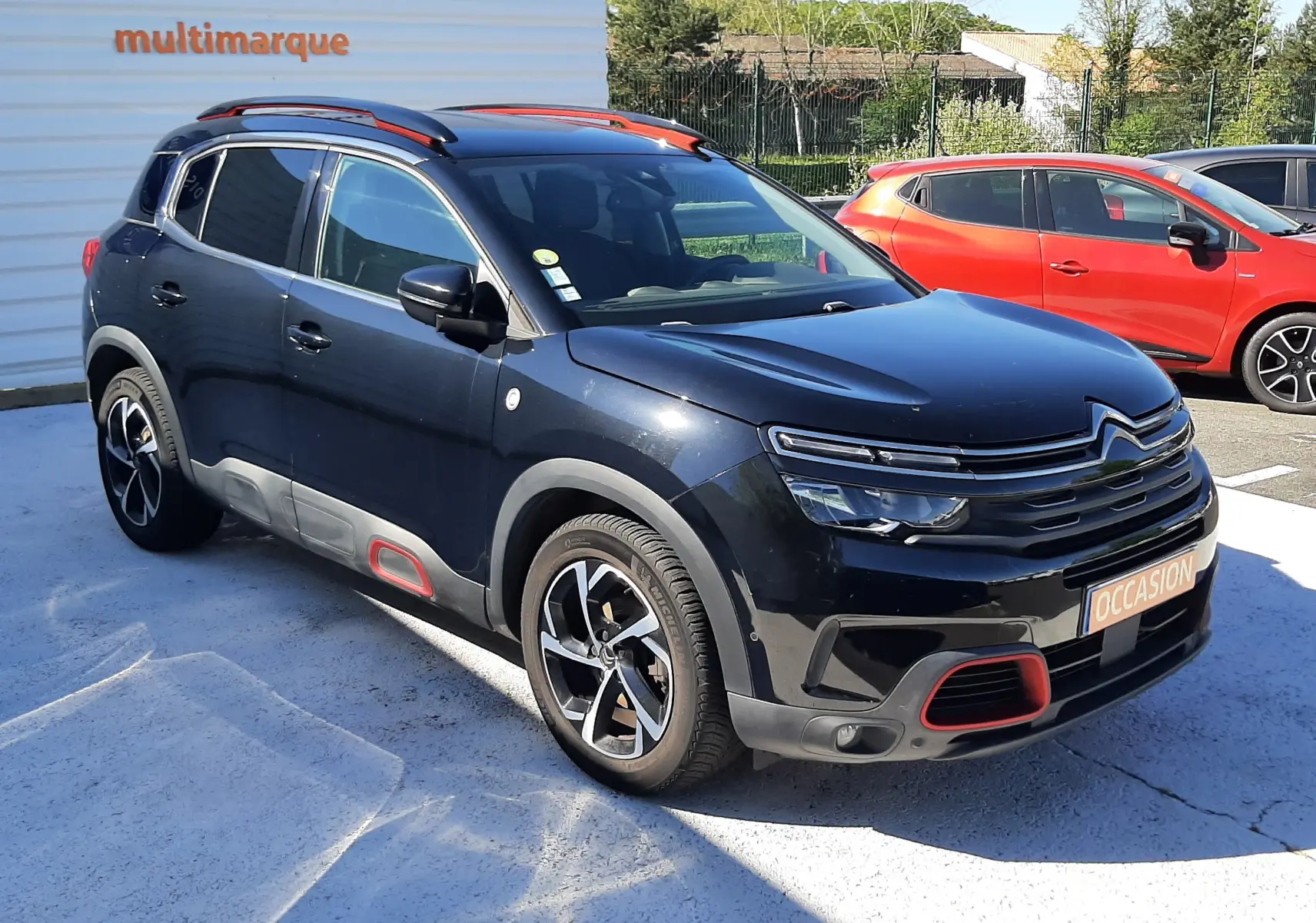 Citroën C5 Aircross noir en 3/4 avant droit, avec détails rouges sur boucliers et jantes bicolores visibles.