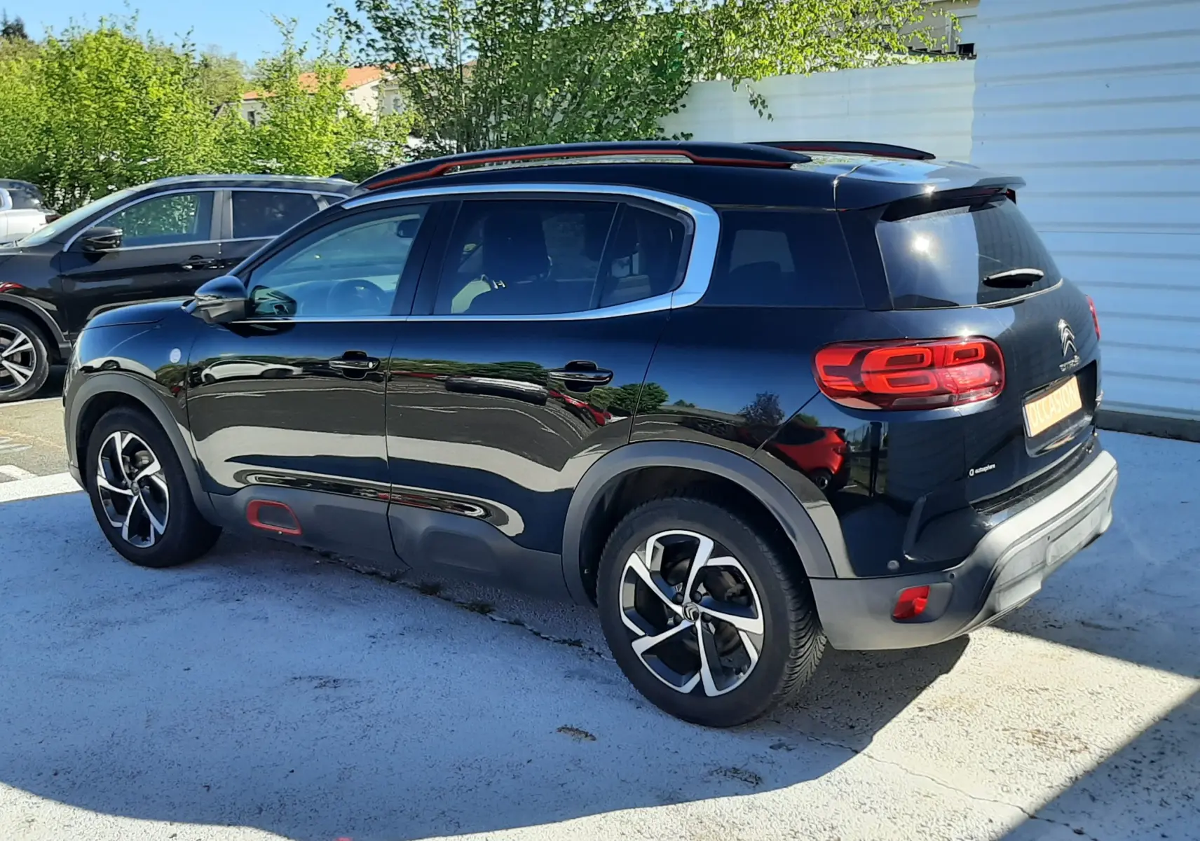 Vue 3/4 arrière droite d'un Citroën C5 Aircross noir avec jantes bicolores et détails rouges sur les protections latérales.