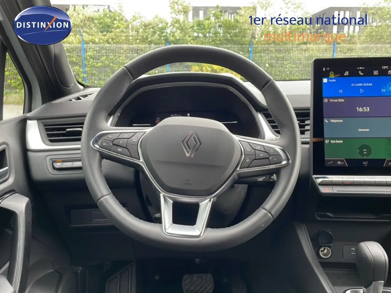 Vue intérieure centrée sur le volant noir Renault avec tableau de bord digital et écran tactile couleur à droite.