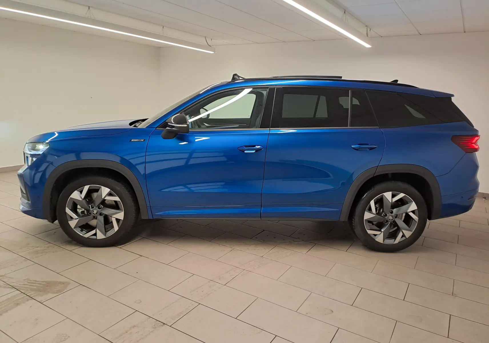 Vue de profil côté gauche d’un Skoda Kodiaq 2025 Bleu RS avec toit panoramique et jantes alliage sport.