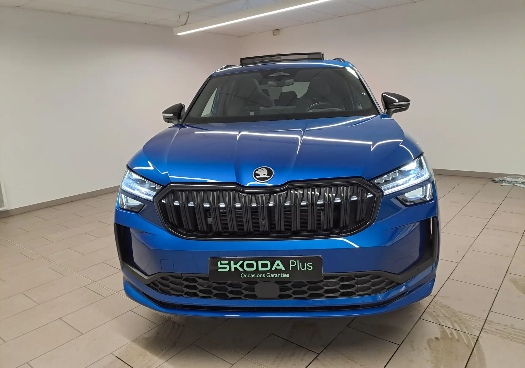 Vue avant d'un Skoda Kodiaq Bleu RS 2025 avec calandre noire et phares LED allumés dans un intérieur neutre.