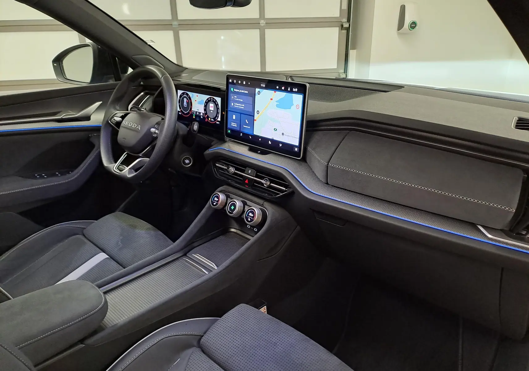 Vue intérieure côté conducteur du Skoda Kodiaq 2025, tableau de bord moderne avec écran tactile central et éclairage d'ambiance bleu.