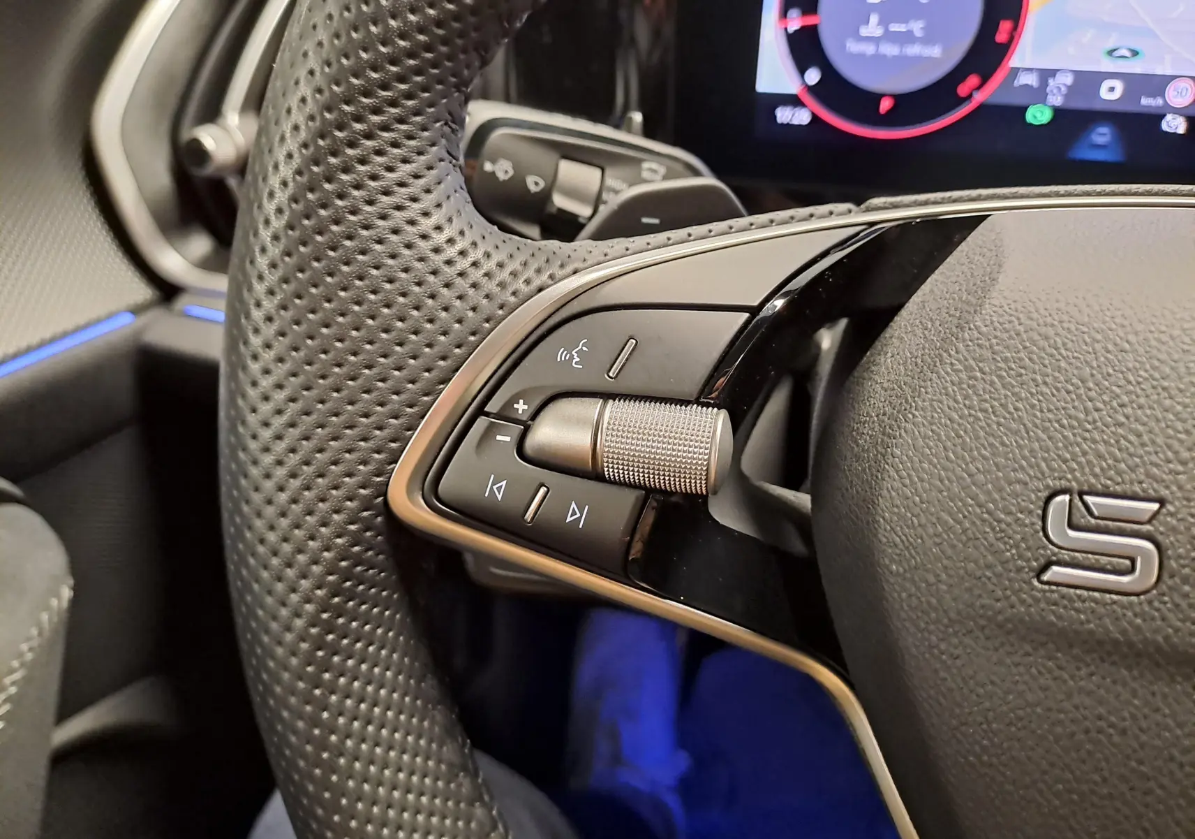 Gros plan sur les commandes gauche du volant perforé du Skoda Kodiaq Bleu RS 2025 avec tableau de bord numérique en arrière-plan.