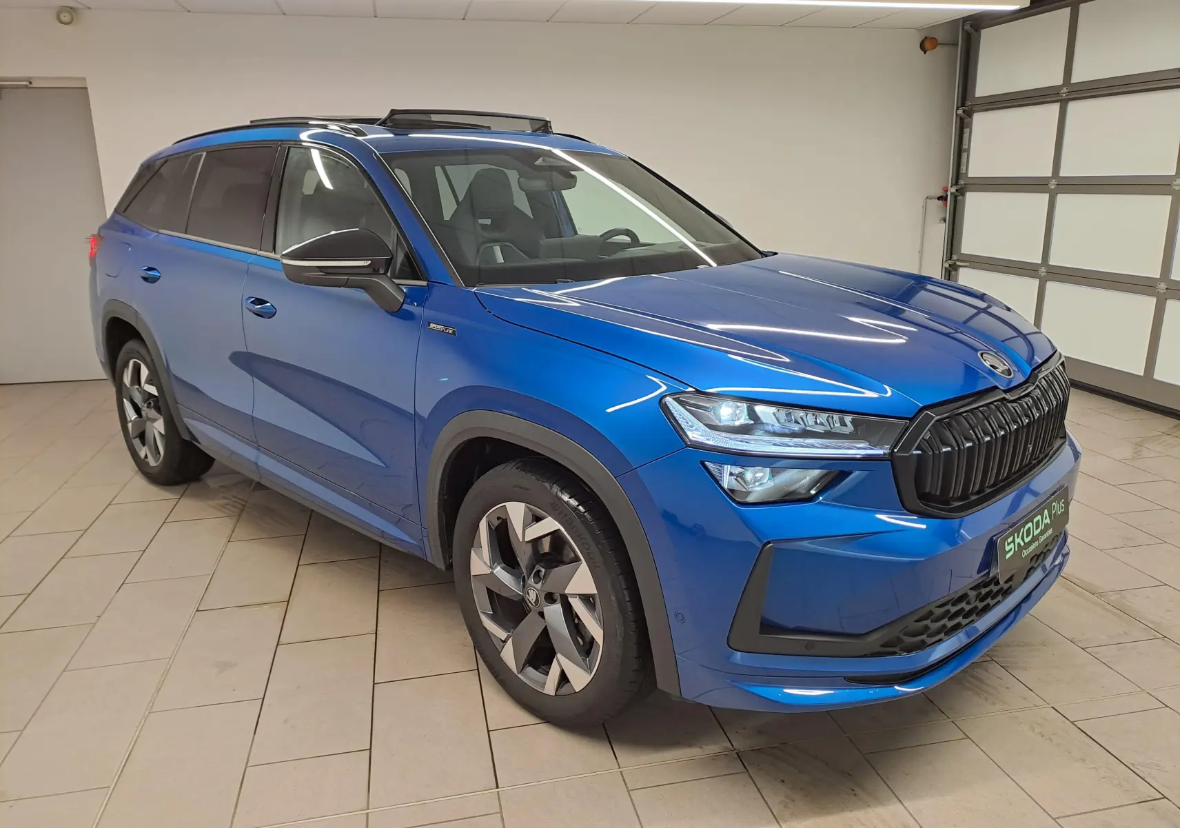 Vue 3/4 avant droite d'un Skoda Kodiaq 2025 bleu RS avec toit panoramique et calandre noire sportive.