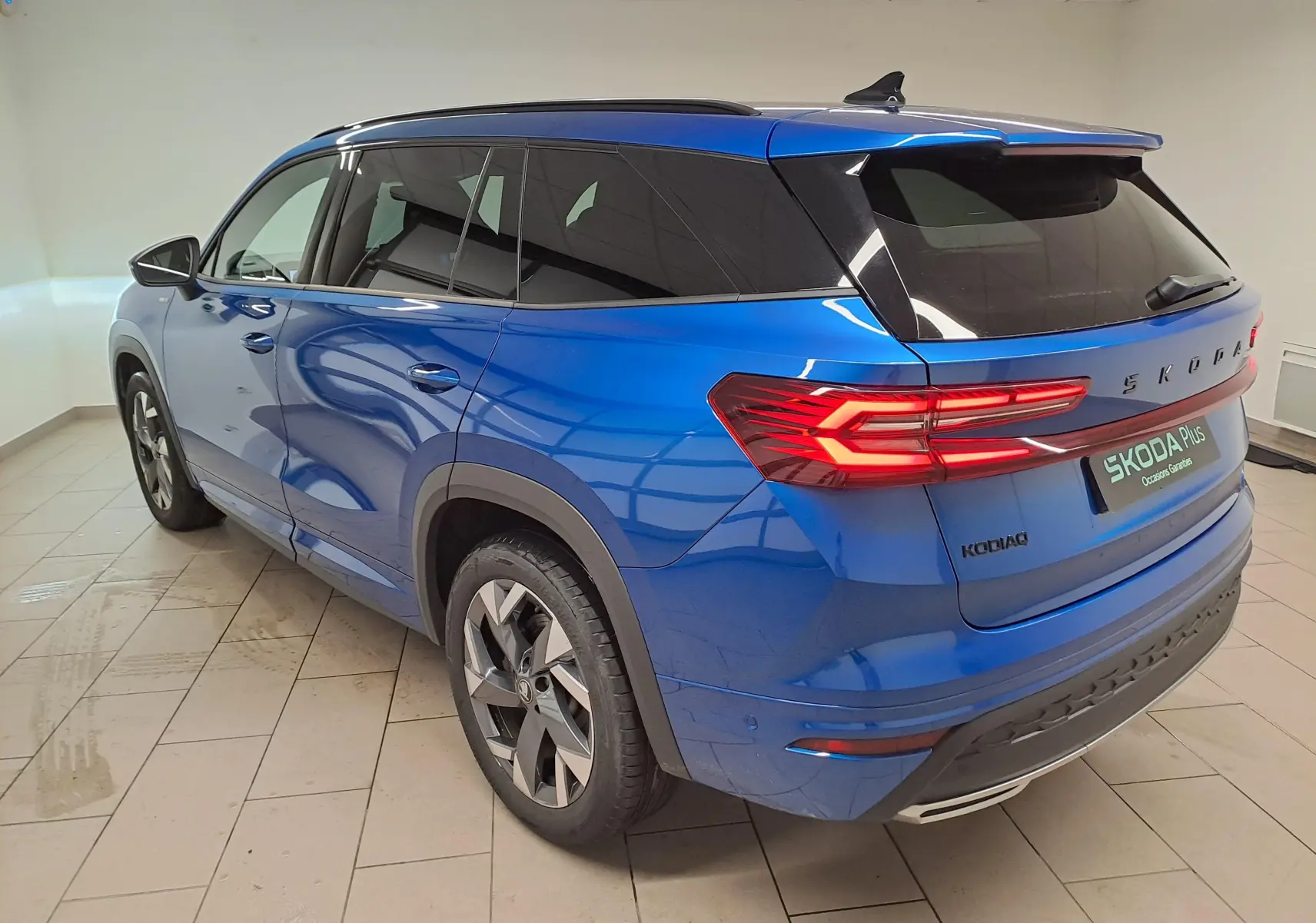 Vue 3/4 arrière droite du Skoda Kodiaq 2025 bleu RS avec toit panoramique et feux arrière LED allumés.