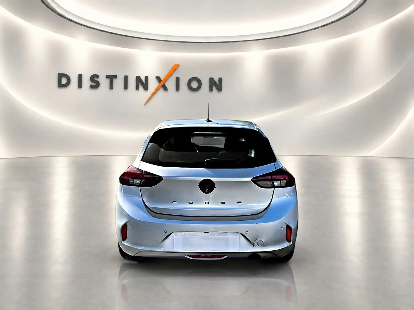 Vue arrière d'une Opel Corsa gris clair 2025 dans un showroom avec logo Distinxion en arrière-plan.