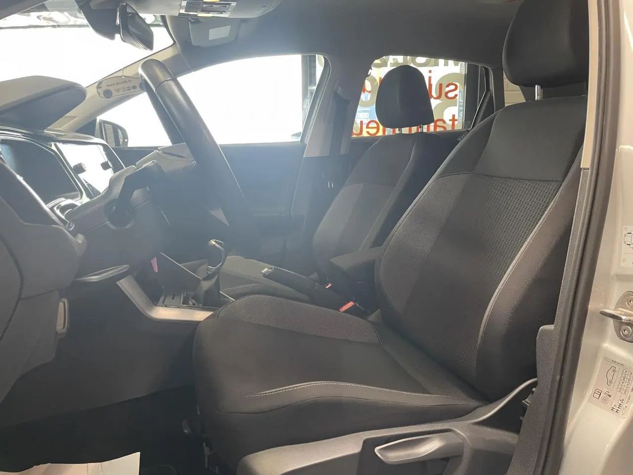 Vue intérieure côté conducteur de la Volkswagen Polo gris clair 2024 avec sièges tissu noirs et volant multifonction.