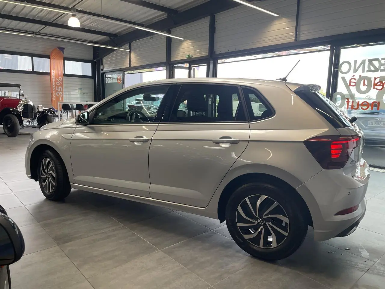 Volkswagen Polo gris clair vue de profil côté gauche en intérieur avec jantes alliage et vitres teintées.
