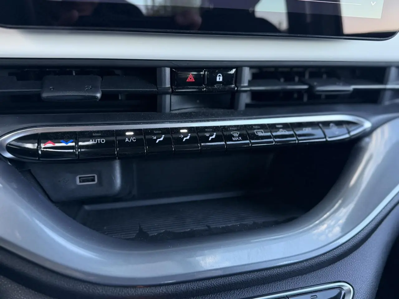 Gros plan sur la console centrale noire de la Fiat 500 électrique blanche, avec commandes de climatisation et prises USB visibles.