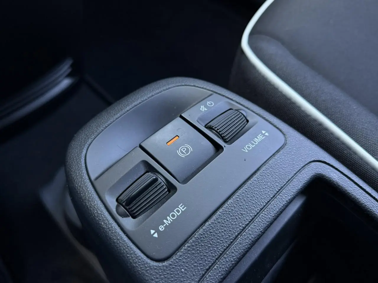 Gros plan sur la console centrale noire avec commandes e-Mode, frein à main électrique et réglage volume du Fiat 500 électrique blanc.