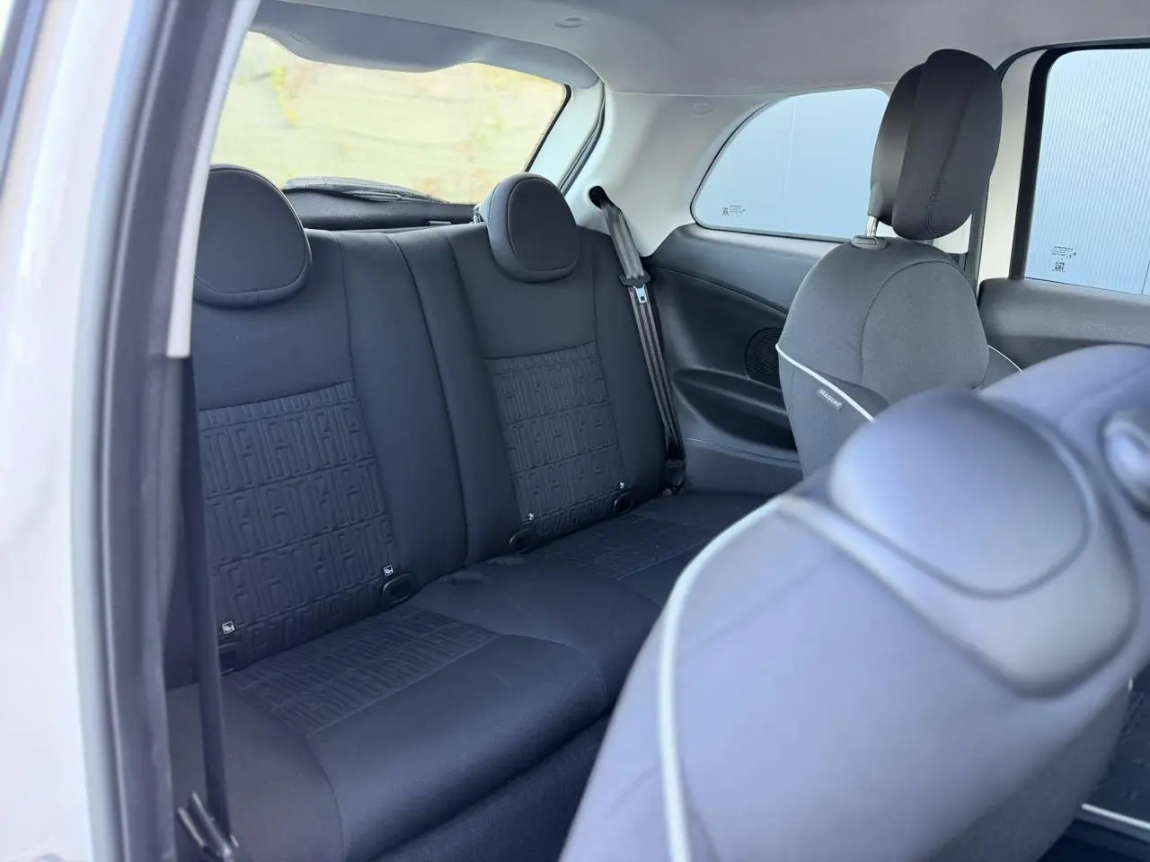 Vue intérieure arrière côté gauche montrant la banquette arrière noire avec motif FIAT sur la Fiat 500 électrique blanche.