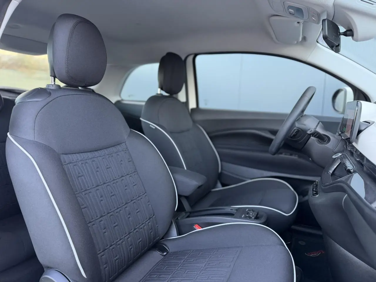 Vue intérieure côté droit de la Fiat 500 électrique 2024 avec sièges tissu noir Seaqual et accoudoir central.