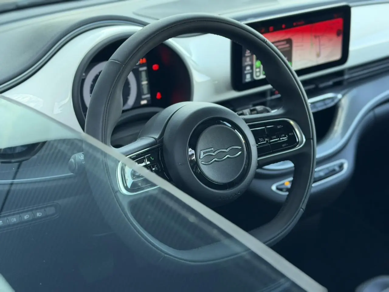 Vue intérieure centrée sur le volant noir et le tableau de bord numérique de la Fiat 500 électrique blanc Artic 2024.