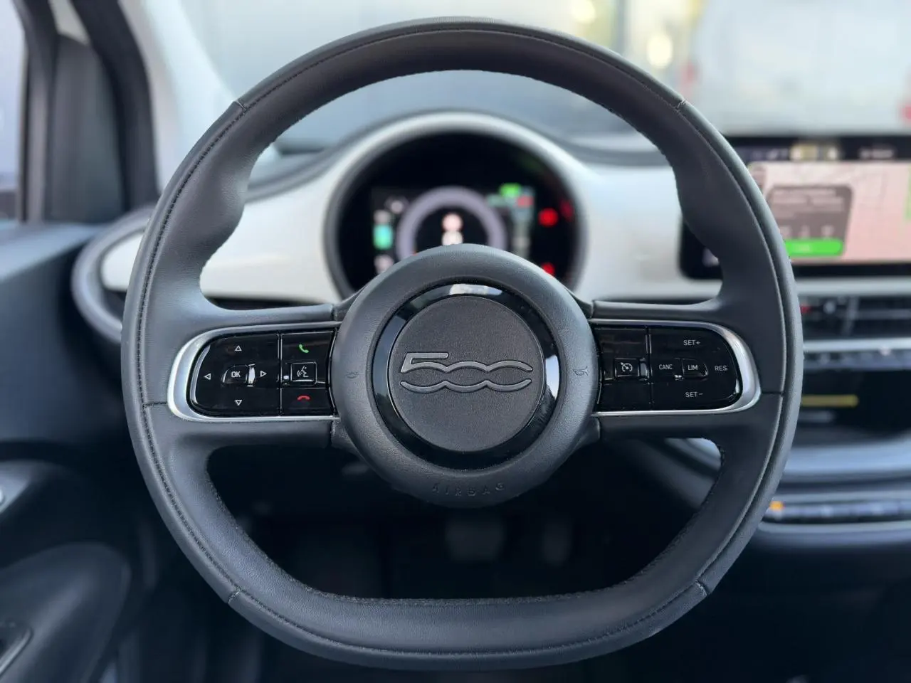 Volant noir Soft-Touch de la Fiat 500 électrique 2024, avec commandes intégrées et tableau de bord numérique en arrière-plan.