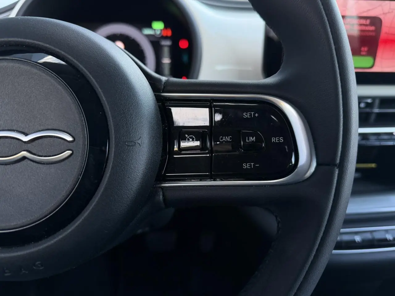 Gros plan sur le volant noir Soft-Touch de la Fiat 500 électrique, avec commandes de régulateur de vitesse visibles.
