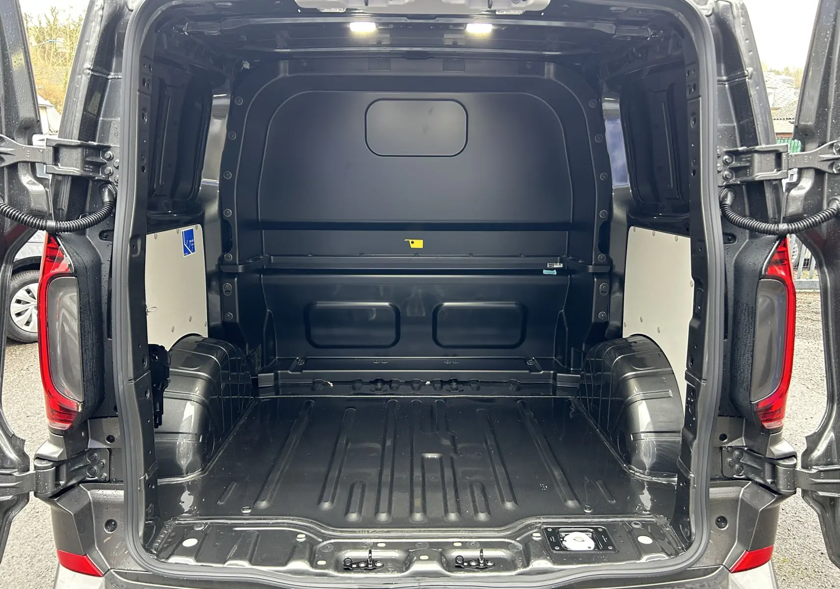 Vue arrière ouverte du Volkswagen Transporter T7 ProCab L1H1 Business en Graphite Dust, montrant l’espace de chargement vide et éclairé.
