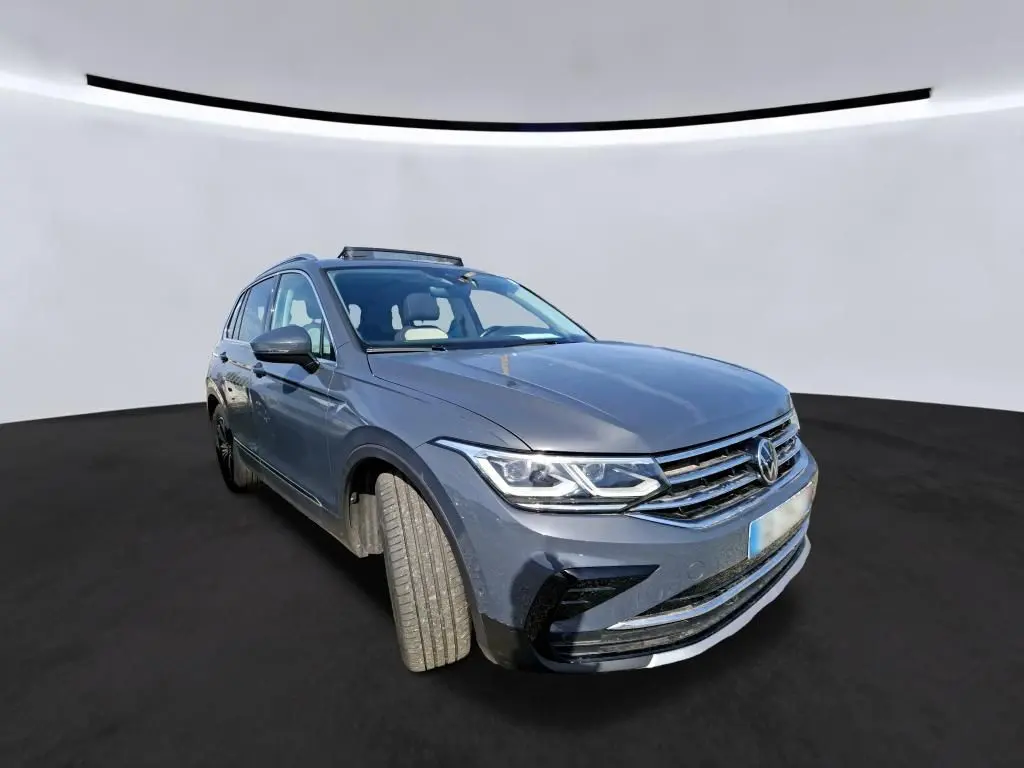 Volkswagen Tiguan gris 3/4 avant droit avec toit ouvrant panoramique visible sur fond neutre.