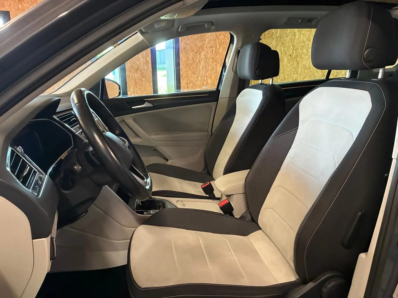 Vue intérieure côté conducteur du Volkswagen Tiguan 2023, sièges bicolores gris clair et noir avec volant cuir.