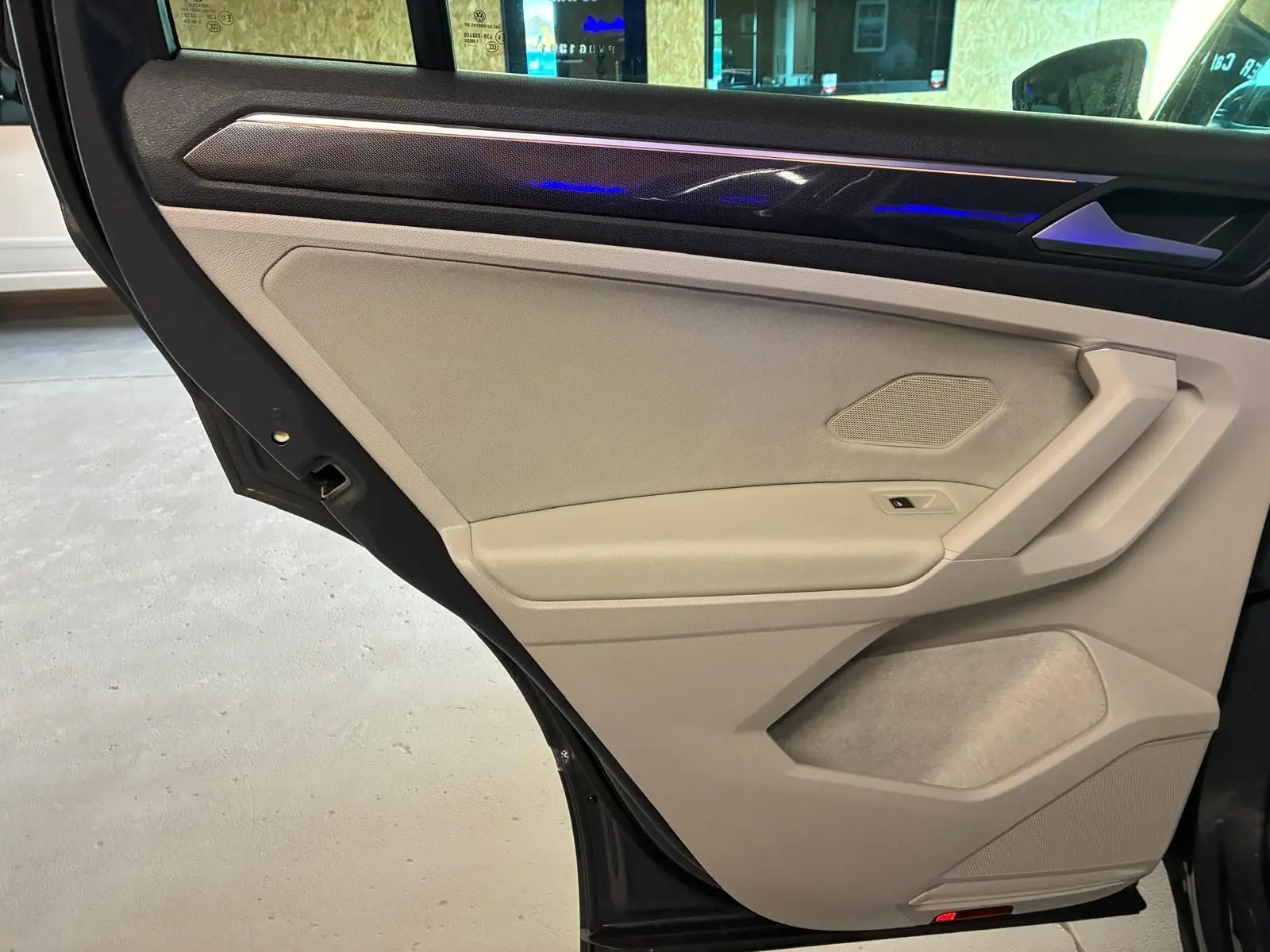 Gros plan sur la porte arrière gauche beige du Volkswagen Tiguan 2023 avec éclairage d'ambiance bleu et habillage textile.