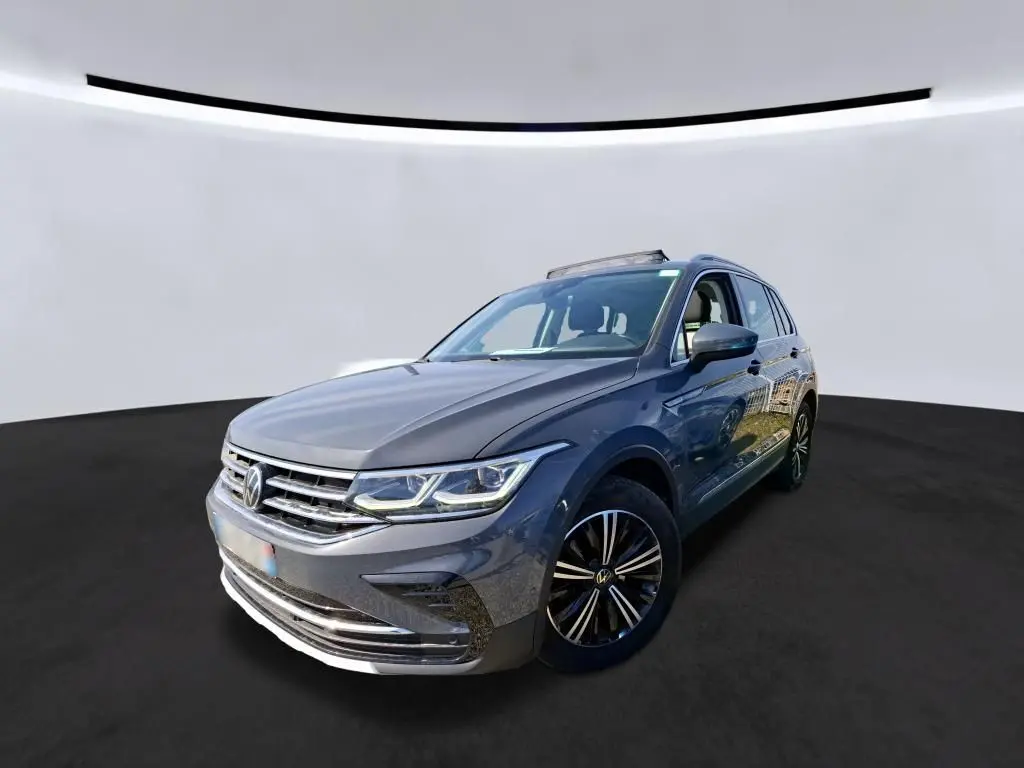 Volkswagen Tiguan gris 3/4 avant droit avec toit ouvrant et jantes noires sur fond neutre.
