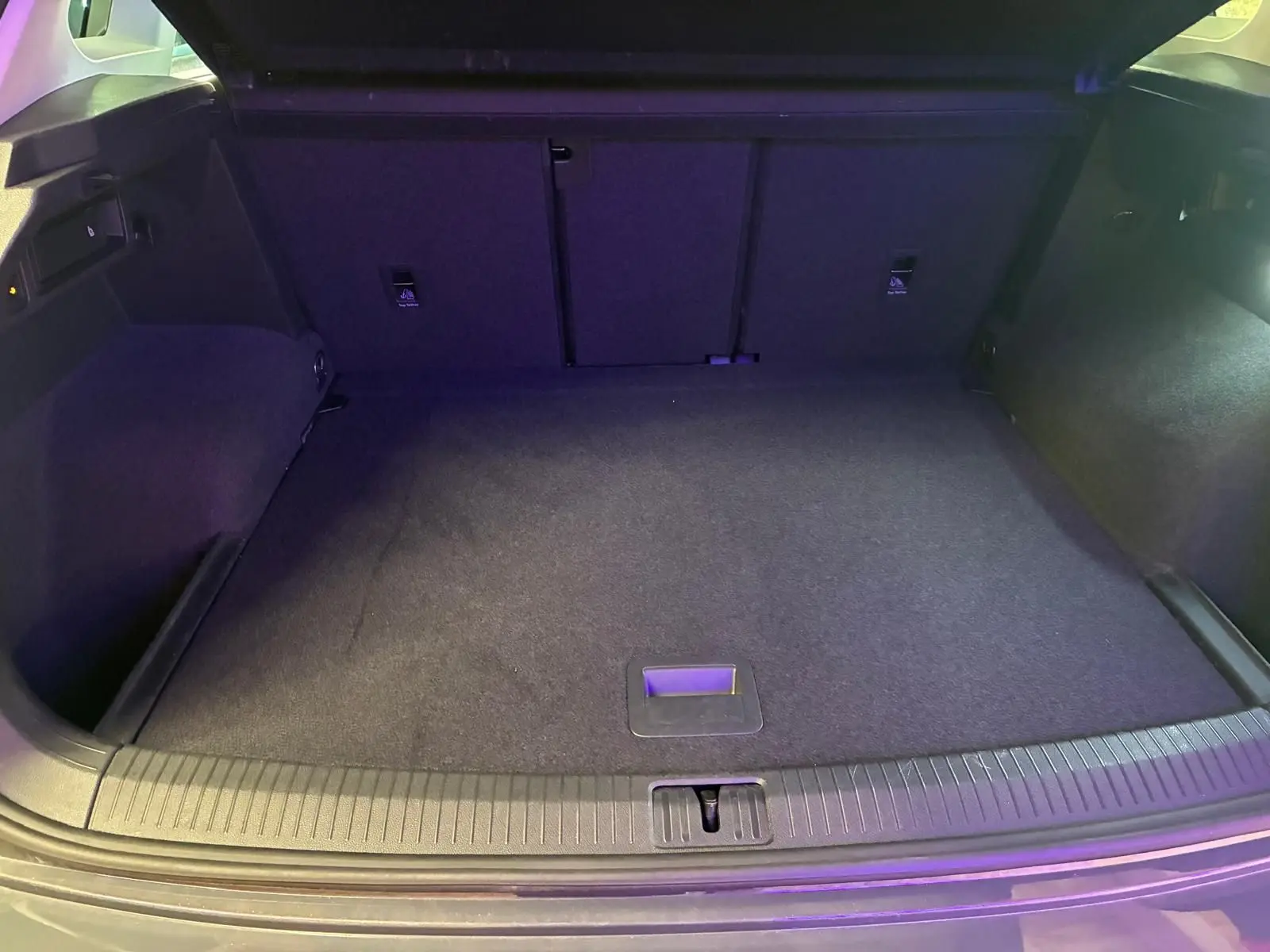 Coffre spacieux du Volkswagen Tiguan 2023 gris, vu de l'arrière avec plancher plat et éclairage intérieur.