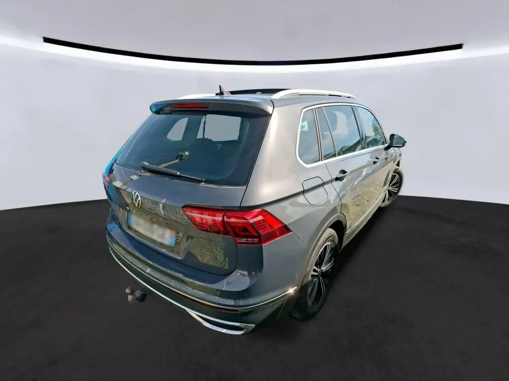 Volkswagen Tiguan gris 3/4 arrière droit avec toit ouvrant panoramique et attelage visible sur fond neutre.