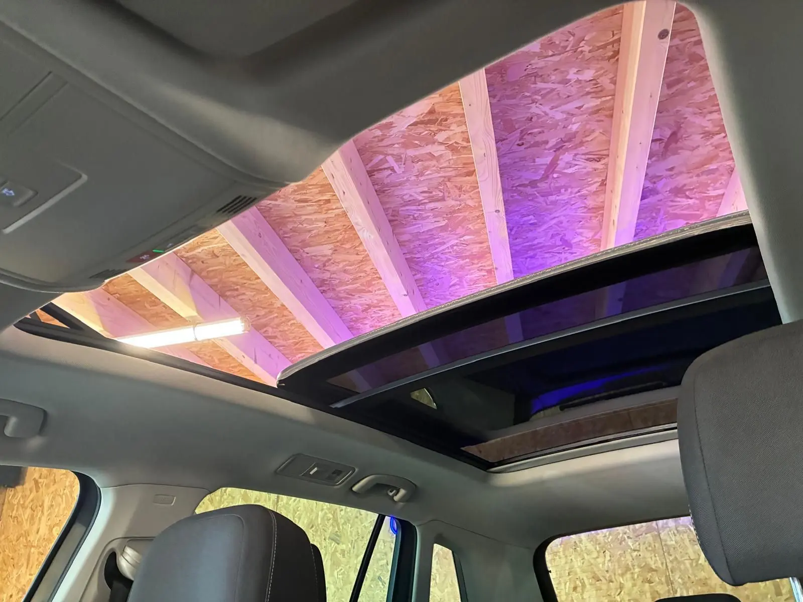 Vue intérieure du toit ouvrant panoramique ouvert du Volkswagen Tiguan gris 2023, avec ciel de toit clair et siège avant visible.