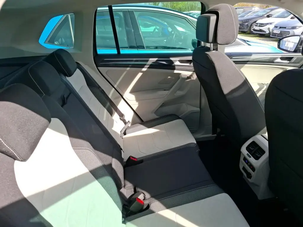 Vue latérale intérieure du siège arrière du Volkswagen Tiguan 2023 gris, montrant les sièges bicolores et la console centrale arrière.